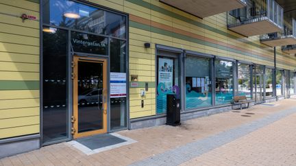 Ingångsdörr i glas på ett hus som är gult med ränder i orange och grönt.