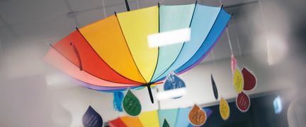 Ett regnbågsfärgat paraply hänger upp och ned från taket. Det händer regndroppsformade lappar med texter från paraplyet.