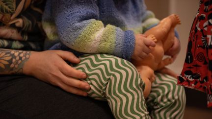 Ett barn sitter i förälders knä och håller en docka. Vi ser inga ansikten.