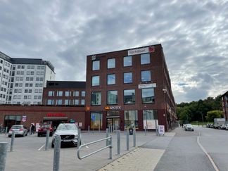 En röd tegelbyggnad med många fönster och en parkering framför.