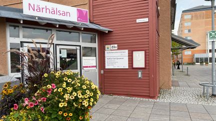 Ingång till rött hus med glasparti. Skylt ovanför dörren med text i rosa: Närhälsn