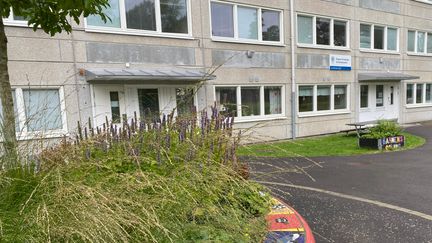 Ett grått höghus med en skylt utanför dörren och en planering framför.