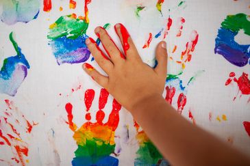 Barnhänder gör handavtryck i regnbågens färger.