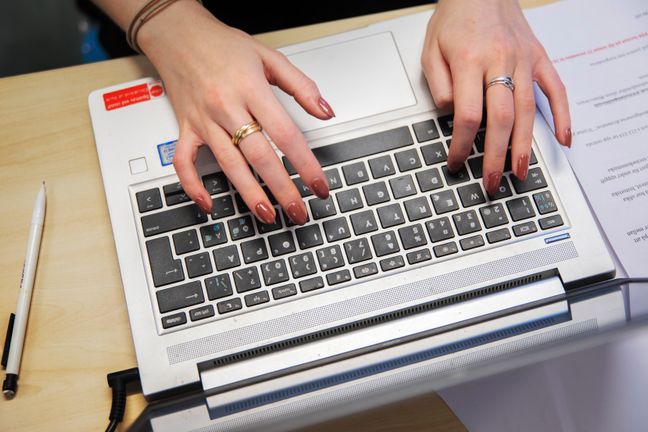 Ett tangentbord på en laptop. Två händer som skriver på tangentbordet syns.