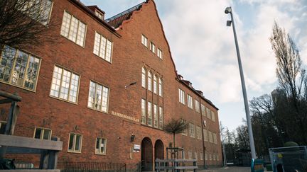 En skolbyggnad i rött tegel med flera stora fönster.