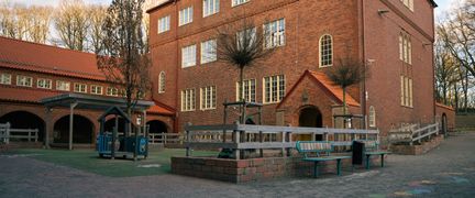 En stor skolbyggnad med en skolgård med en lekställning framför.