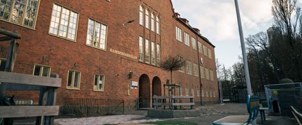 En skolbyggnad i rött tegel med flera stora fönster.
