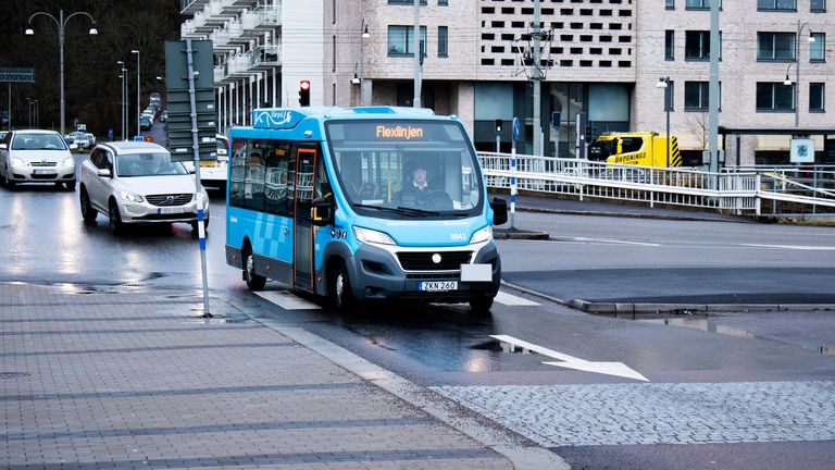 En blå liten flexlinjebuss kör mot kameran. Två bilar kommer bakom.