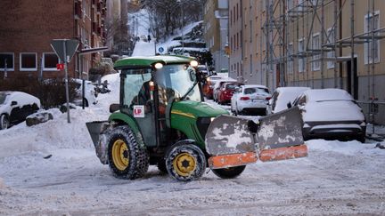 En grön traktor med plog plogar en snötäckt gata.