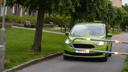 Grön färdtjänstbil kör mot en stängd bom på en innergård.
