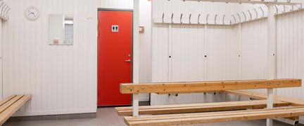 Omklädningsrum med ljusa väggar, bänkar och krokar