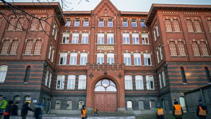 En grupp elever som står på skolgården framför en en stor skolbyggnad i rött tegel.