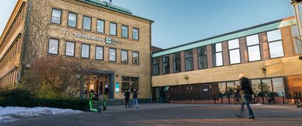 En överblick av Santosskolans skolgård och huvudbyggnad med några personer i bakgrunden.