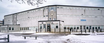 Jättestensskolans huvudbyggnad med skolans skylt och några bänkar i bakgrunden.