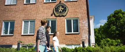 Tre elever som går förbi skolbyggnaden. - Foto av Welcom