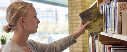 Foto av en elev som tar en bok ur en bokhylla i biblioteket. - Foto av Welcom