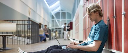 Foto av en elev som sitter med sin skoldator på golvet i skolkorridoren - Foto av Welcom