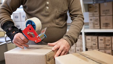 En person tejpar igen lådor i en lagerlokal.