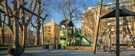 En lekplats med en grön rutschkana och en byggnad i bakgrunden.