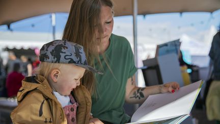 En vuxen och ett barn sitter i ett evenemangstält och läser en bok.
