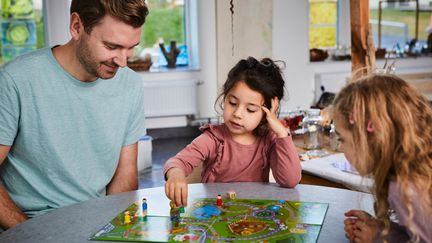 En pedagog och två barn sitter vid ett bord i en förskola och spelar spel.