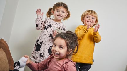 ett barn som sitter och två barn som står i bakgrunden och klappar
