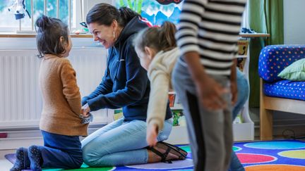 En vuxen sitter på knä framför ett barn, skrattar och busar med barnet.
