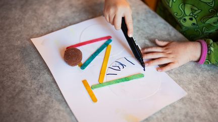 Barnhänder som målar en cykel på ett papper.