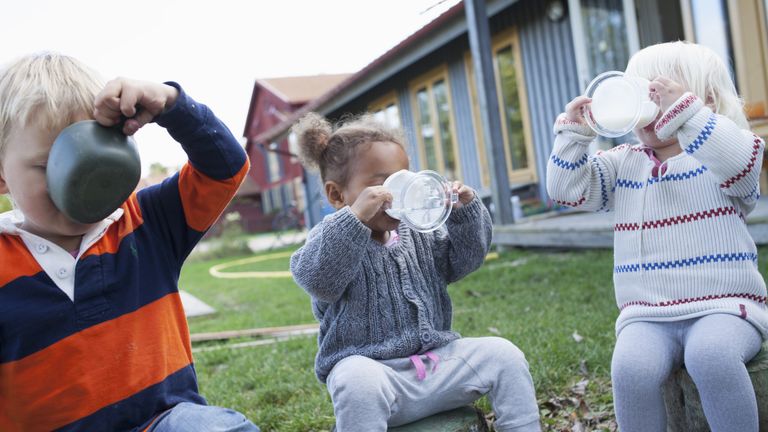 Tre barn sitter utomhus och dricker ur varsin mugg.