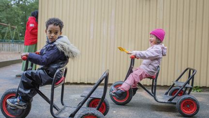 Två barn som sitter på trehjular utomhus