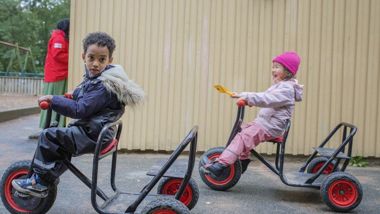 Två barn som sitter på trehjular utomhus
