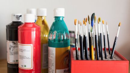 Flaskor med målarfärg och penslar som står på tork.