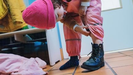 Ett barn i ytterkläder böjer sig fram för att dra ner overallen på benet.