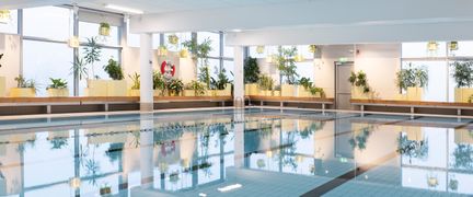 Bassäng i Hammarbadet sedd från ett av hörnen. De bortre väggarna är av glas och längs väggarna står stora gröna växter.