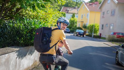 Pappa på cykel med litet barn bakpå. 