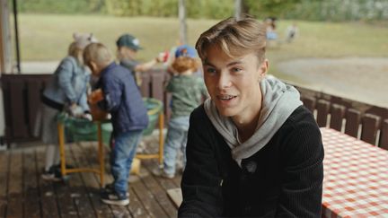 Ung kille som ler med småbarn i bakgrunden