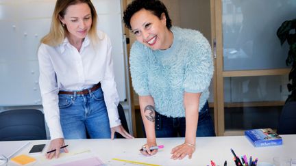 Två kvinnor vid bord med pennor och papper