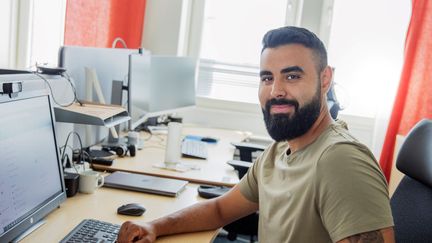 En man som sitter vi sitt skrivbord och ler