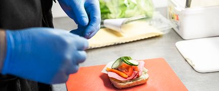 En person med blå handskar gör en smörgås.