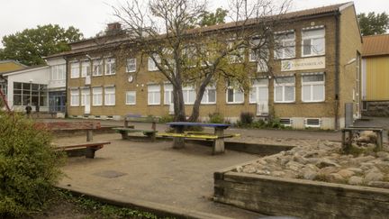 En sandlåda med bänkar och en skolbyggnad i gult tegel i bakgrunden