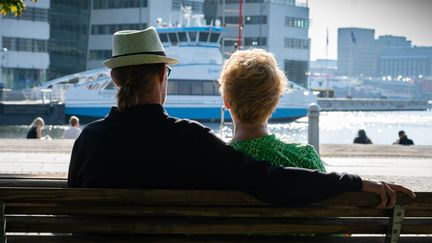 Två personer sitter på en bänk med ryggen mot kameran. Den ena personen har armen runt den andre.