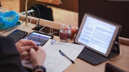 En persons skrivbord på sammanträde. Hen har en frukt, ett vattenglas, läsplatta och dokument framför sig.