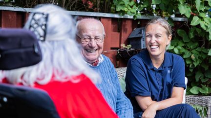 Medarbetare sitter på en bänk i solen med två äldre personer