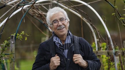 En man med grått hår och glasögon står i en trädgård, ler och tittar in i kameran.