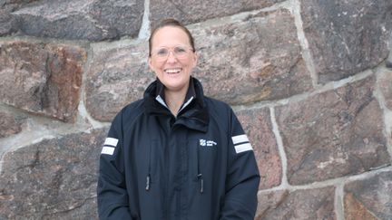 Porträttbild av sjuksköterskan Cecilia som står utomhus framför en stenvägg. Hon tittar in i kameran och ler.