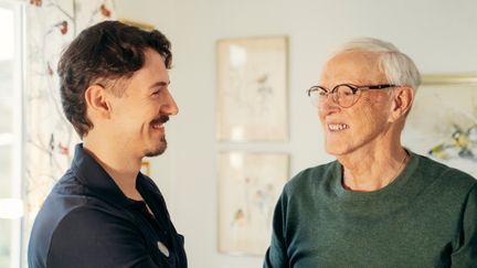 Två personer, en arbetsterapeut och en omsorgstagar står bredvid varandra, de båda ler.