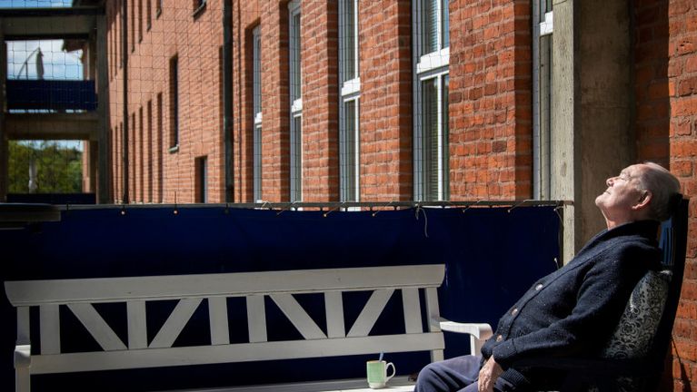 En man sitter mot en tegelvägg solar ansiktet.