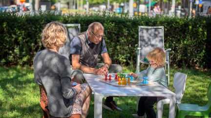 Två vuxna och ett barn spelar spel i skuggan av ett träd.