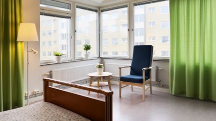Rum med hörnfönster. Vid fönstret står en fåtölj och ett litet bord..