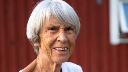 En äldre kvinna tittar in i kameran och ler